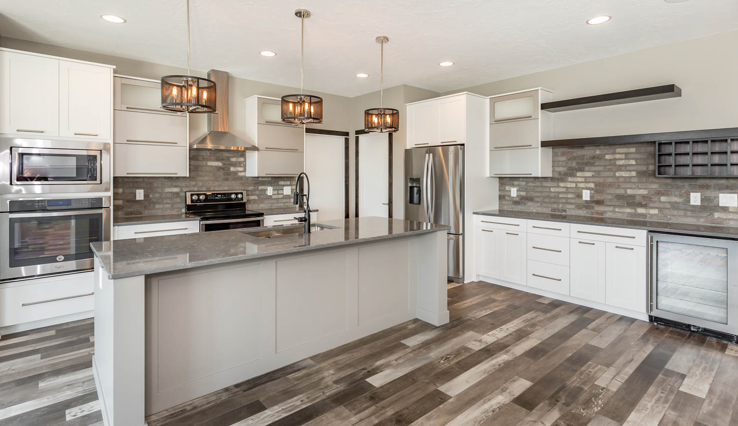 UPH kitchen with white cabinets, grey counter tops, brick backsplash, stainless steel appliances and pendant lighting over island